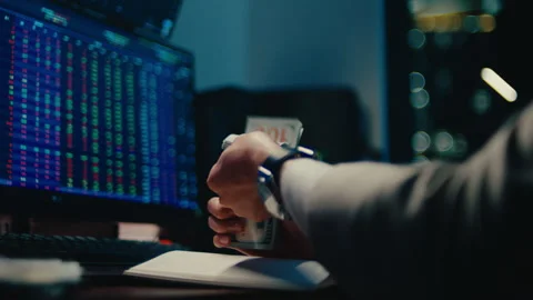 Successful stock trader holding stack of cash in front of financial charts 動画素材 329087194
