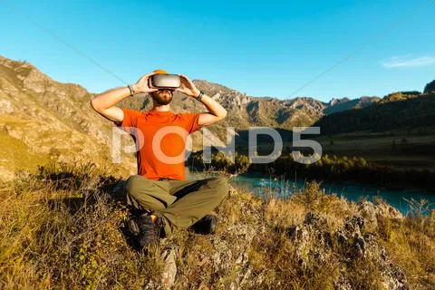 Successful young man, using virtual reality goggles to tour in mountains, on Stock Photos
