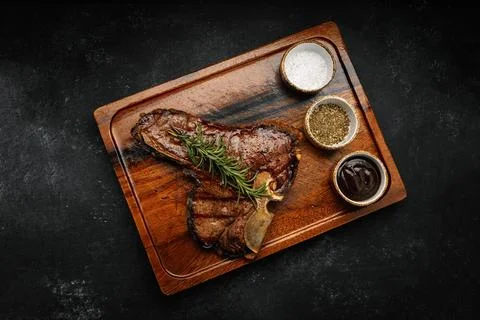 Succulent grilled T-bone steak with rosemary and spices served on dark wood.. Stock Photos