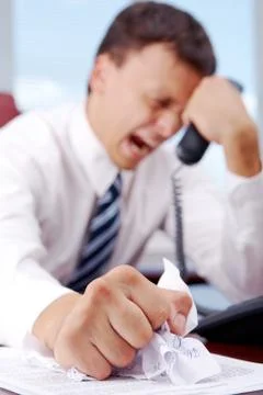 Suffering businessman crumpling document while holding phone receiver 写真素材