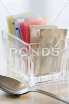 Sugar and sweetener packets next to spoon Stock Photos