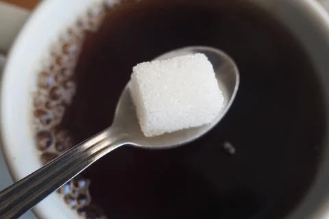 Sugar cube on a spoon above a cup of black coffee Stock Photos