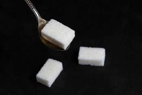 Sugar cube on a spoon. Spoon over a pile of sugar. Stock Photos