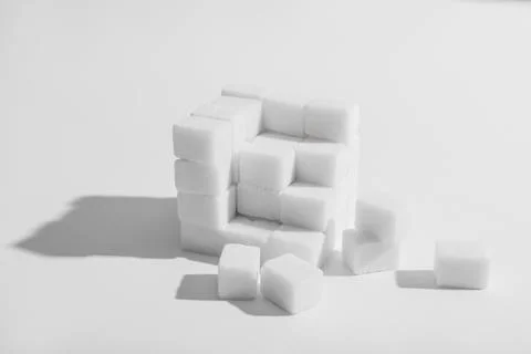 Sugar cubes arranged in a cube shape with scattered pieces, sweetness and unh Stock Photos