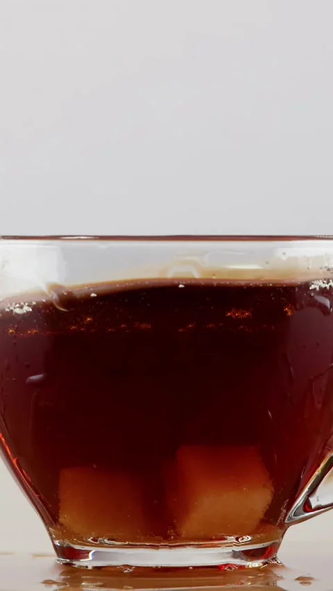 Sugar Cubes Dropping into Glass Cup of Black Tea Causing Splash Stock Footage 346267418