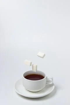 Sugar cubes fall into a cup of tea on a white background. A cup of tea with refi Stock Photos