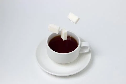Sugar cubes fall into a cup of tea on a white background. A cup of tea with refi Stock Photos