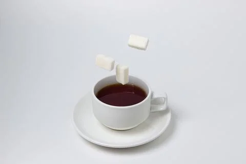 Sugar cubes fall into a cup of tea on a white background. A cup of tea with refi Stock Photos