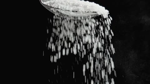 Sugar is falling down from silver spoon at black background. 库存影片 329938504