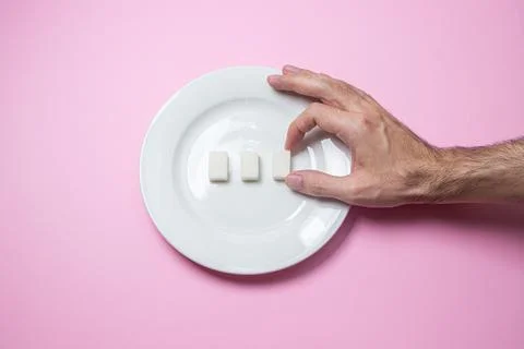 Sugar on a pink background. Three cubes of sugar on a white plate.  Stock Photos