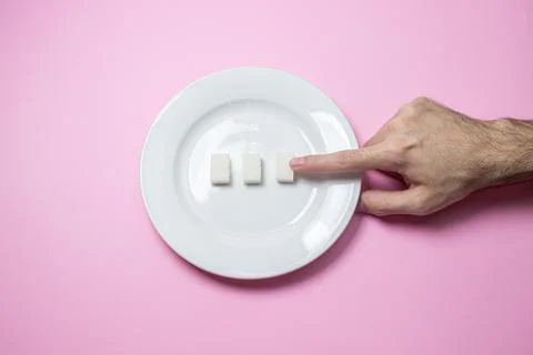 Sugar on a pink background. Three cubes of sugar on a white plate.  Stock Photos