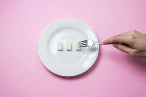 Sugar on a pink background. Three cubes of sugar on a white plate.  Stock Photos