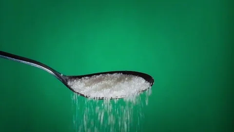 Sugar pouring from a spoon on green background Video stock 71263652