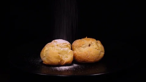 Sugar powdering of couple eclairs, rotating on black background to the right Stock Footage 74929563