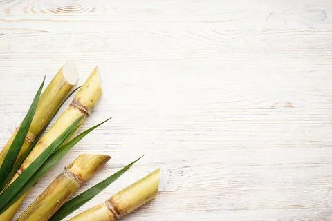 Sugarcane and green leaf on rustic white table, space for text. Top view. Stock Photos