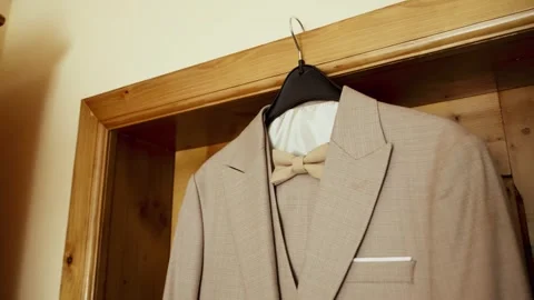 A suit with a bow tie is hanging on a hanger inside a wooden door frame. Stock Footage 345642928