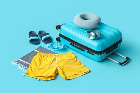 Suitcase with swimming trunks and beach accessories on blue background Stock Photos