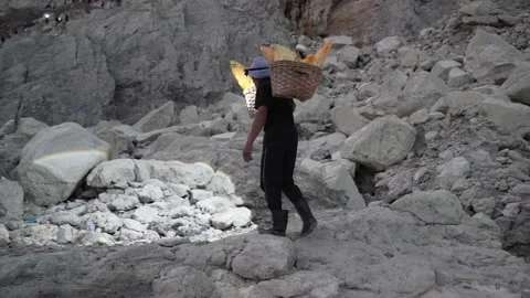 Sulfur Miner Walking With Baskets in Rocky Volcanic Landscape of Ijen, East Java Stock Footage 334035344