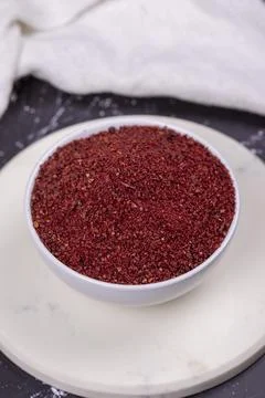 Sumac on dark background. Dried ground red Sumac powder spices in wooden bowl Foto stock