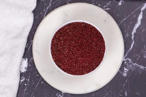 Sumac on dark background. Dried ground red Sumac powder spices in wooden bowl Foto stock