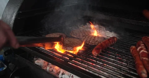Summer barbecue BBQ cook flips flame grilled burger and hot dog sausages Stock Footage 334076367