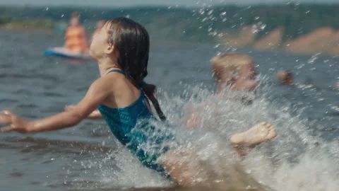 Summer beach and fun. Kids have fun and jump into the river from the sandy beach Stock Footage 343795325