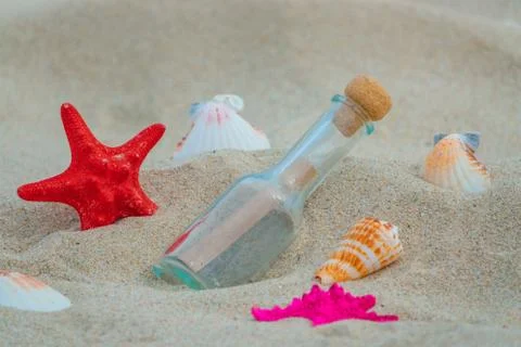 Summer beach concept. Bottle with message on the beach with starfish and shells. Stock Photos