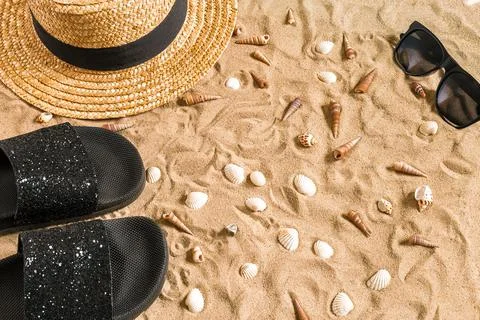 Summer beachwear, flip flops, hat, sunglasses and seashells on sand beach. Stock Photos