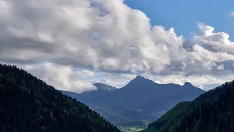 In summer, clouds spill over mountain peaks in a wooded basin Stock Footage 167839299