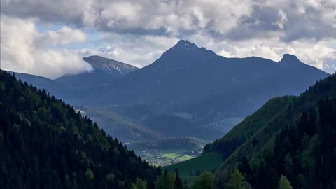 In summer, clouds spill over mountain peaks in a wooded basin Stock-Footage 167958476