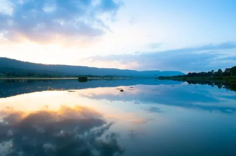 Summer is coming. The sun setting through the clouds around the lake and moun Stock Photos