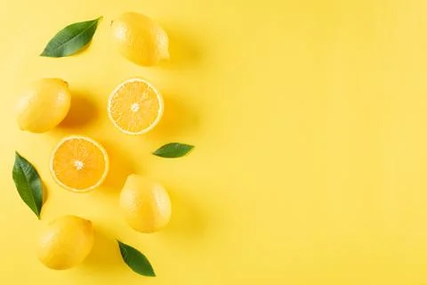 Summer composition made from oranges, lemon and green leaves on pastel yellow Stock Photos