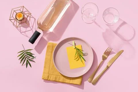 Summer dinner party table setting with rose wine bottle, pink plate, and gold Stock Photos