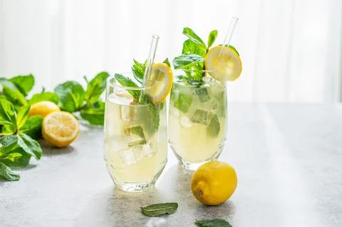 A summer drink with lemon, mint, and ice in a two glasses against a sunny w.. Stock Photos