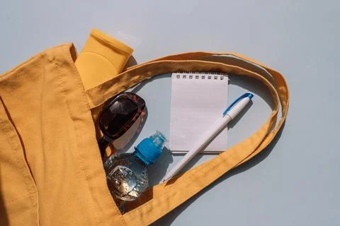 Summer essentials in yellow tote bag with water bottle, sunglasses and notepad Foto stock