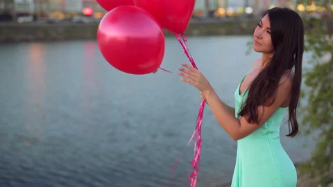 Summer. Evening. Girl in long green dress posing with red air balloons Stock Footage 85597853