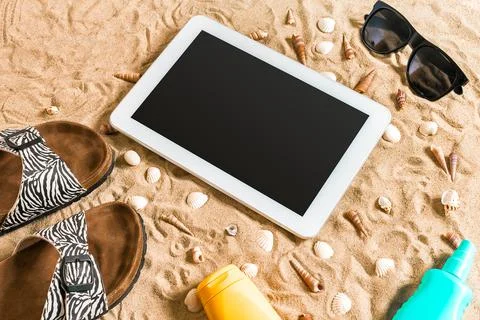 Summer flip-flops, tablet, sunglass and seashell on sand. With place for your Stock Photos
