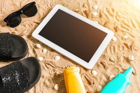 Summer flip-flops, tablet, sunglass and seashell on sand. With place for your Stock Photos