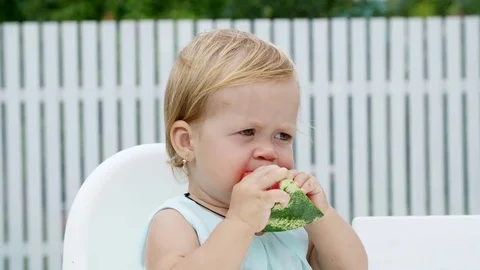 Summer, in the garden, funny one-year-old blond girl eating watermelon Stock Footage 80439856
