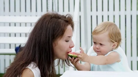 Summer, in the garden, a funny one-year-old blonde girl treats her mother with Stock Footage 80440008