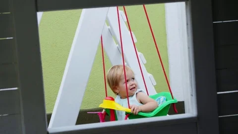 Summer, in the garden, nice little one year-old girl swinging on a swing in the Stock Footage 80438757