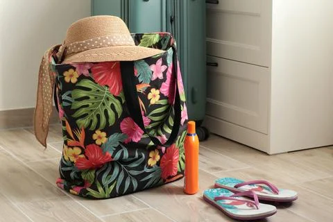 Summer hat with bow on beach bag near flip flops at home. Summer and vacation Stock Photos