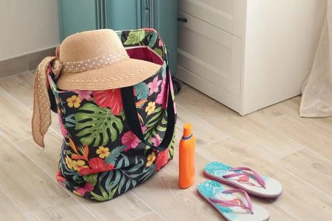 Summer hat with bow on beach bag near flip flops at home. Summer and vacation Stock Photos