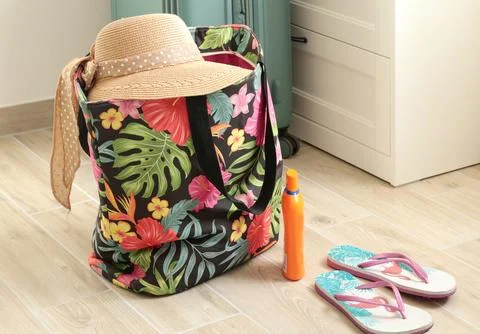 Summer hat with bow on beach bag near flip flops at home. Summer and vacation Stock Photos