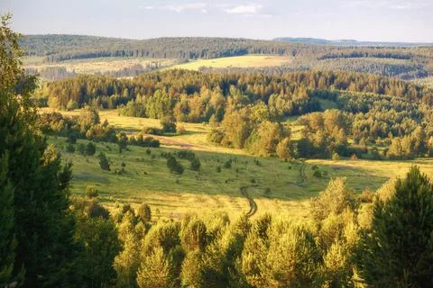 Summer landscape in the mountains, with forest, fields, road and the cloudy sky 写真素材