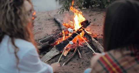 Summer night on the sand beach by the ocean, the bright burning fire, two girls 库存影片 135613599