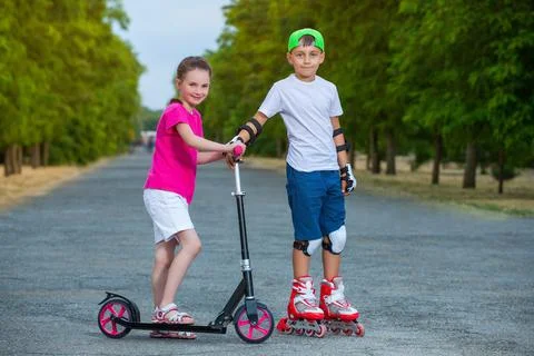 In the summer in the park the boy rolls on rollers and the girl rolls on a sc Foto stock