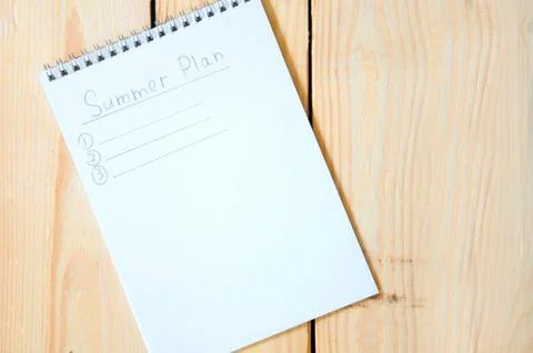 Summer Plan. Notepad with entries for summer plans on a wooden background. Stock Photos