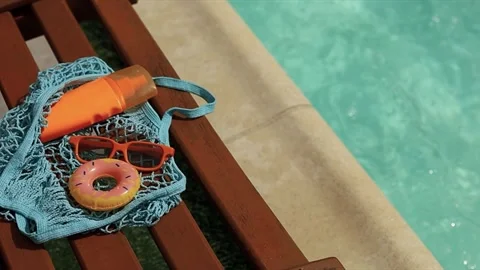 Summer pool vibes: mesh bag with sunscreen, sunglasses, and toy float on lo.. Stock Footage 334318571