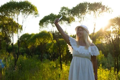 In the summer, in the rays of the setting sun, a cute woman in a white sundress Stock Photos